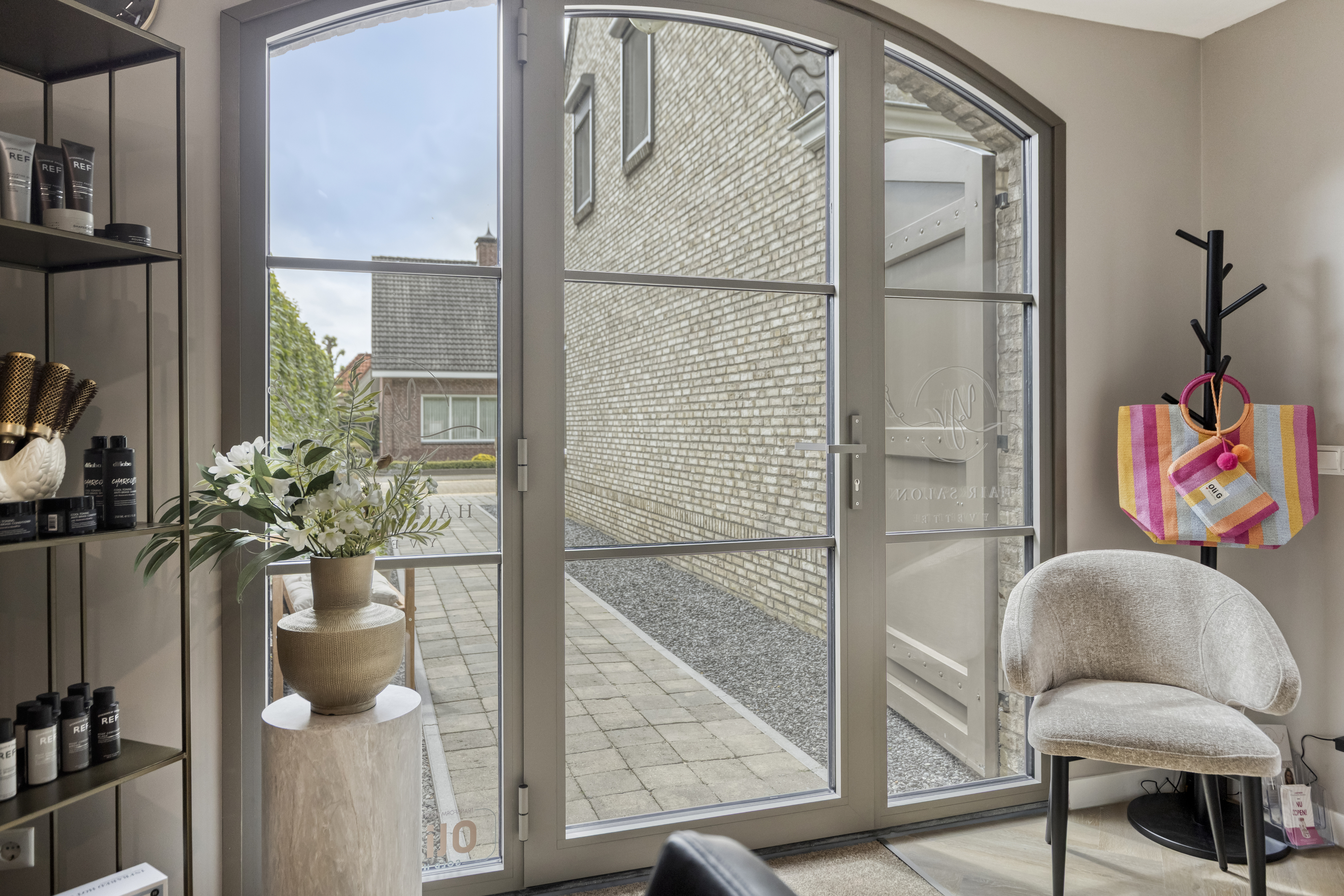 De afbeelding toont een moderne glazen deur met een strak metalen frame, die naar een buitenpatio leidt. De deur heeft grote glazen panelen die natuurlijk licht binnenlaten. Het ontwerp is minimalistisch, met nadruk op strakke lijnen en functionaliteit.