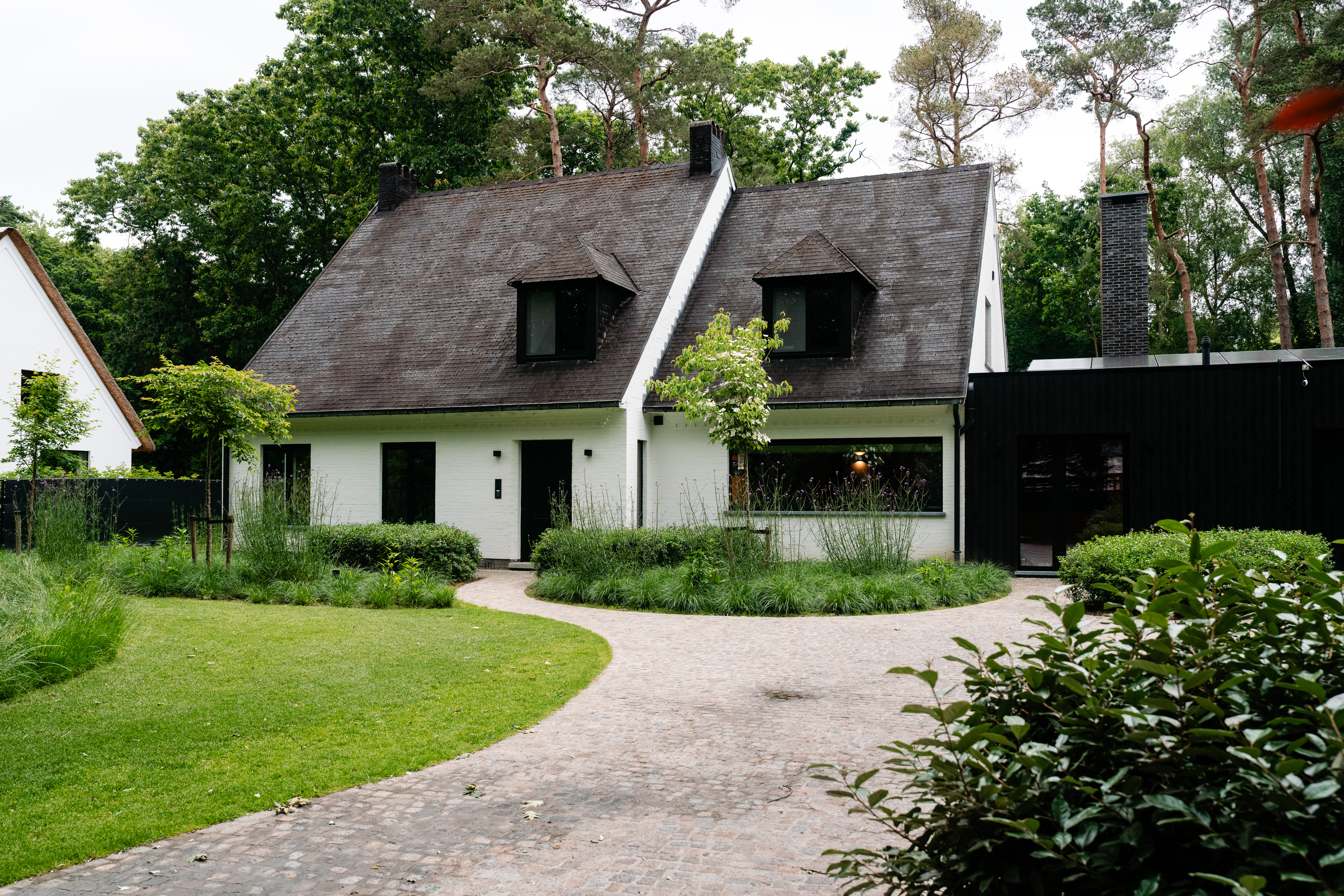 Het huis heeft een charmant ontwerp met zwartomrande ramen en een centrale deur. De ramen zijn symmetrisch geplaatst, wat de esthetische aantrekkingskracht vergroot. De voordeur is stevig en past bij de algehele uitstraling van het huis.