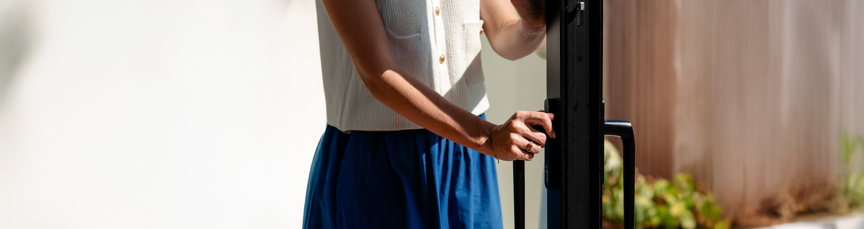 De afbeelding toont iemand die een modern schuifraam opent. Het raam heeft een strak zwart frame en een groot glazen paneel, waardoor natuurlijk licht binnenkomt. De handgreep is ergonomisch, ontworpen voor een gemakkelijke grip en soepele bediening.