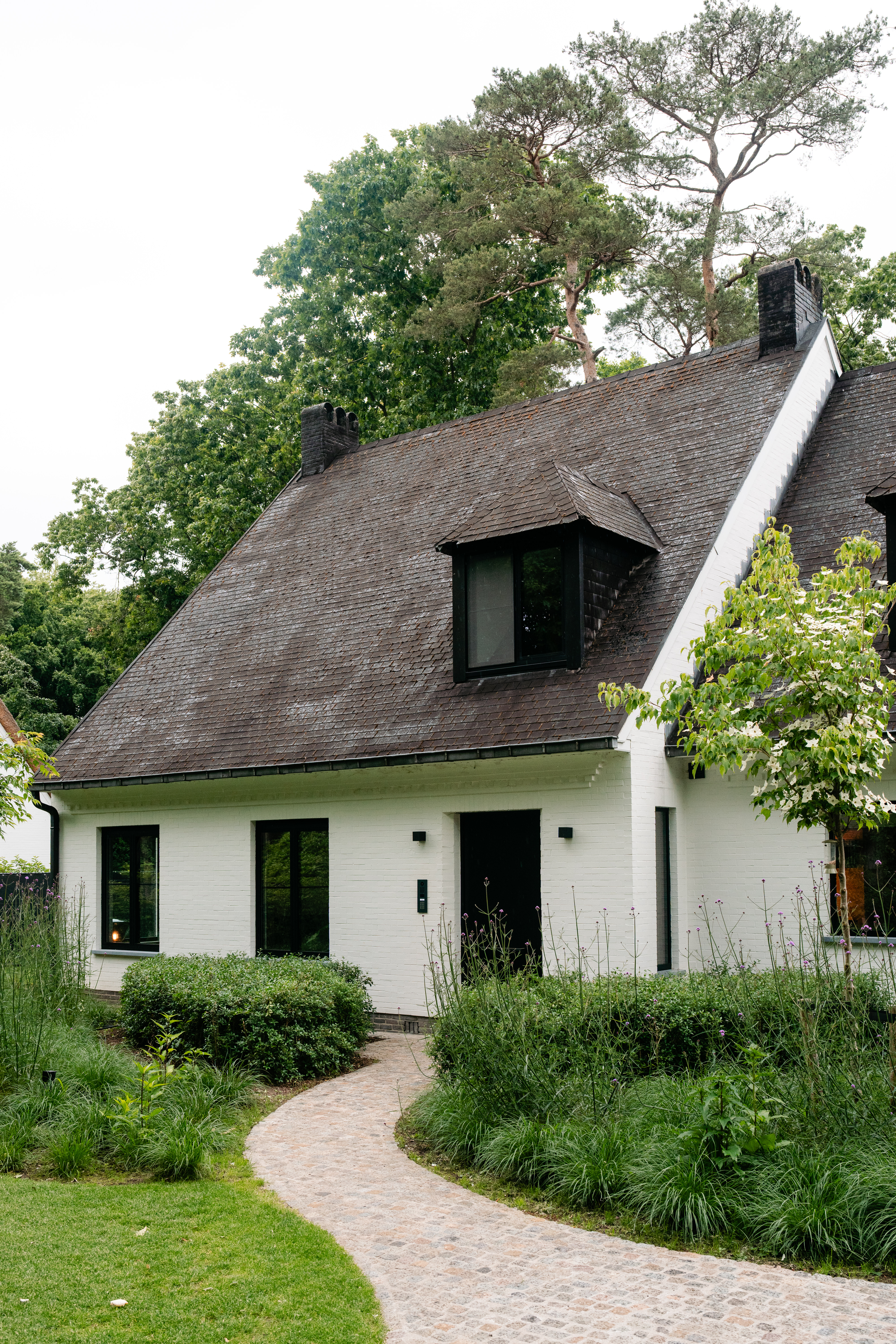 Het huis heeft een charmant ontwerp met zwartomrande ramen en een centrale deur. De ramen zijn symmetrisch geplaatst, wat de esthetische aantrekkingskracht vergroot. De deur is eenvoudig maar elegant, en past goed bij het geheel.