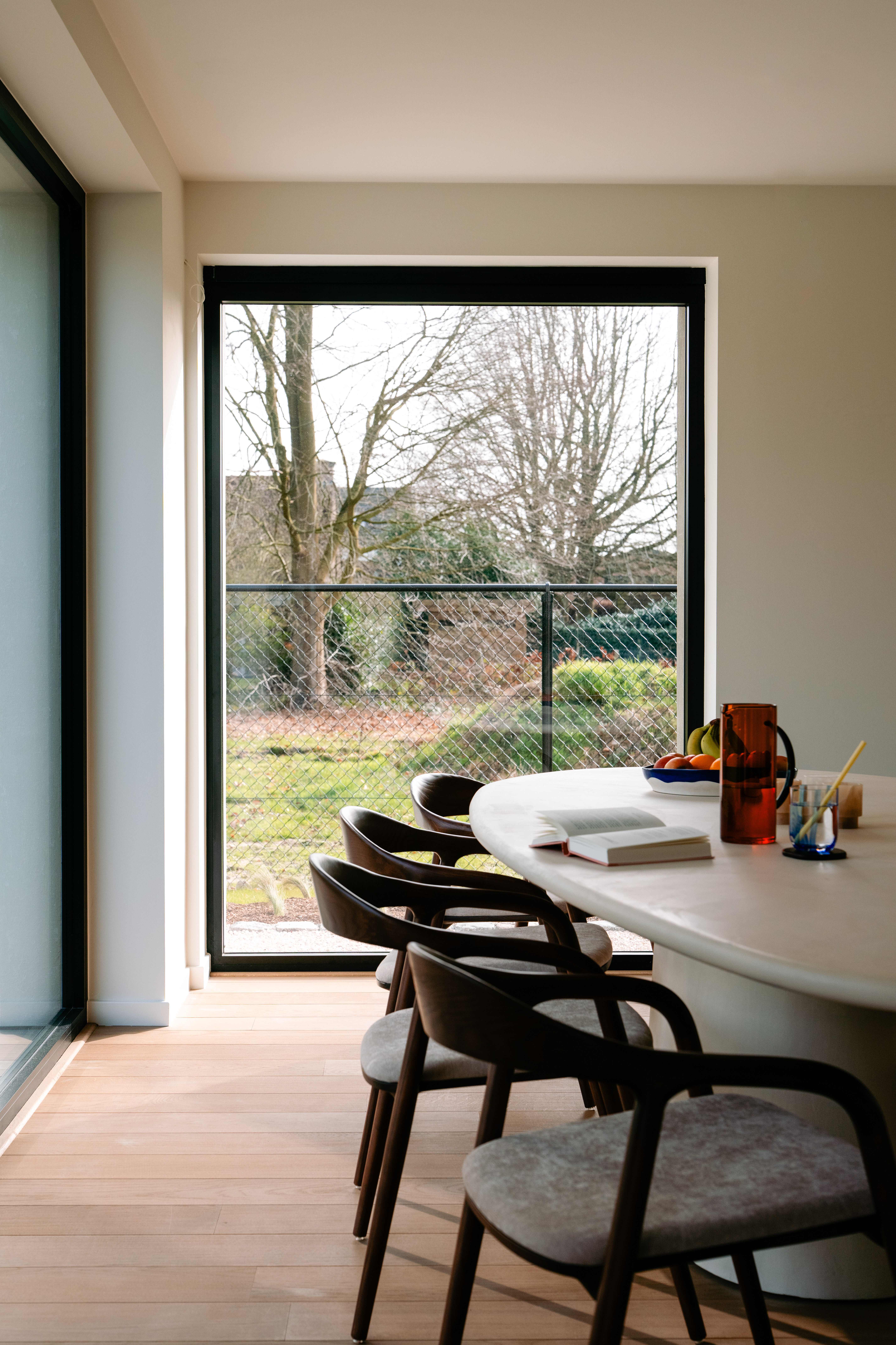 L'image montre un intérieur moderne avec de grands châssis coulissants qui laissent entrer beaucoup de lumière naturelle. Les châssis offrent une vue dégagée sur le jardin, créant une connexion fluide entre l'intérieur et l'extérieur. Le design épuré des châssis complète la décoration minimaliste de la pièce.