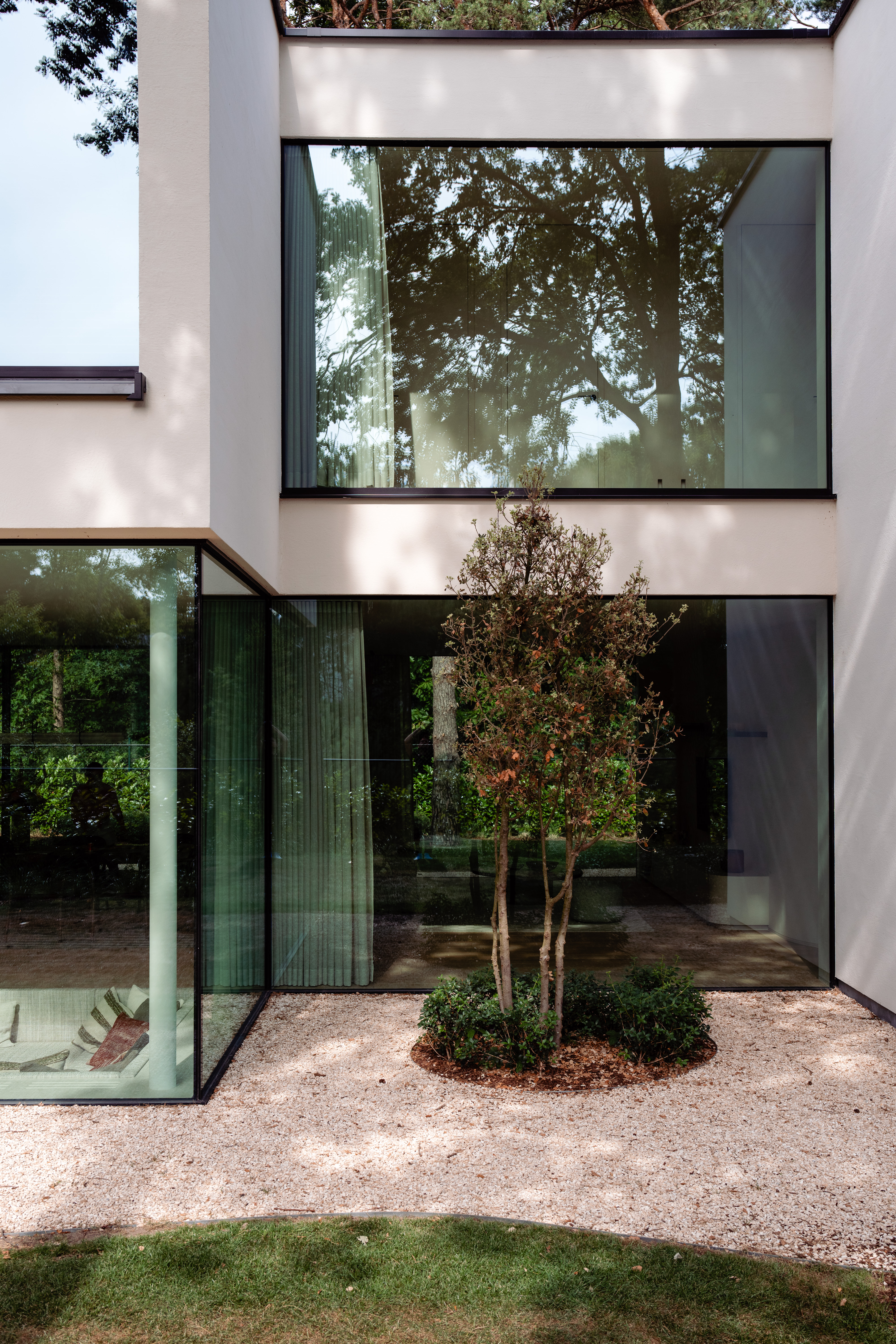 Het moderne huis heeft grote glazen ramen die een naadloze verbinding met buiten bieden. De ramen zijn van vloer tot plafond, waardoor natuurlijk licht het interieur overspoelt. Het strakke ontwerp vult de minimalistische architectuur aan, met strakke lijnen en een neutraal kleurenpalet. De deuren zijn geïntegreerd in de glazen panelen, waardoor de esthetische continuïteit behouden blijft.