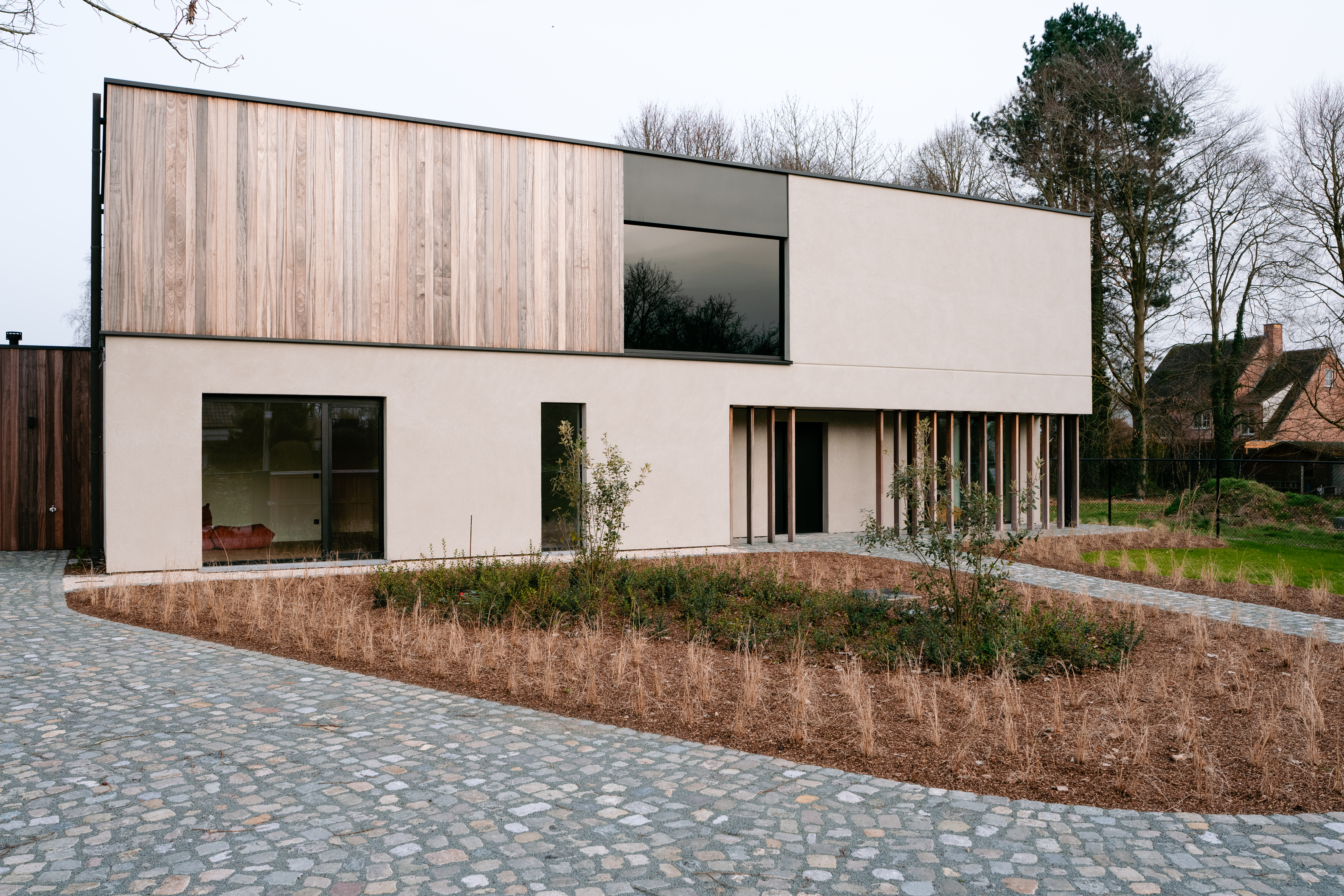 Het moderne huis heeft grote, rechthoekige ramen en een strakke deur, wat het minimalistische ontwerp versterkt. De ramen zijn strategisch geplaatst om natuurlijk licht binnen te laten, terwijl de deur de strakke lijnen van het gebouw aanvult.